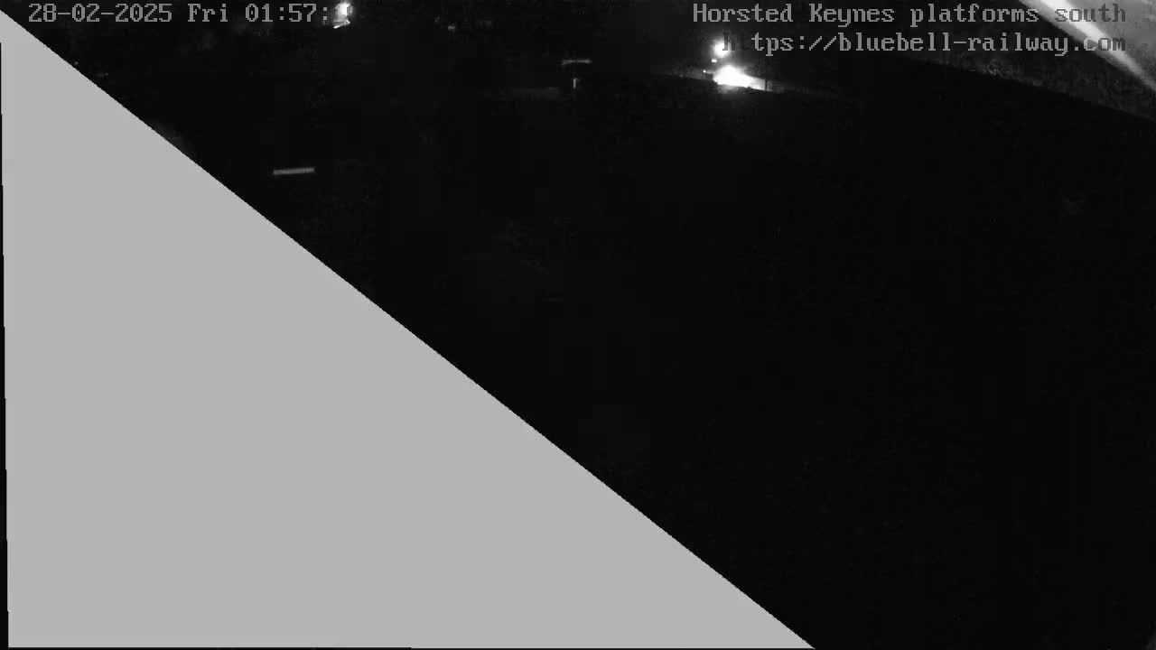 A nighttime, low-light image shows a dark area, possibly a railway platform, with a gray triangle obscuring part of the view.