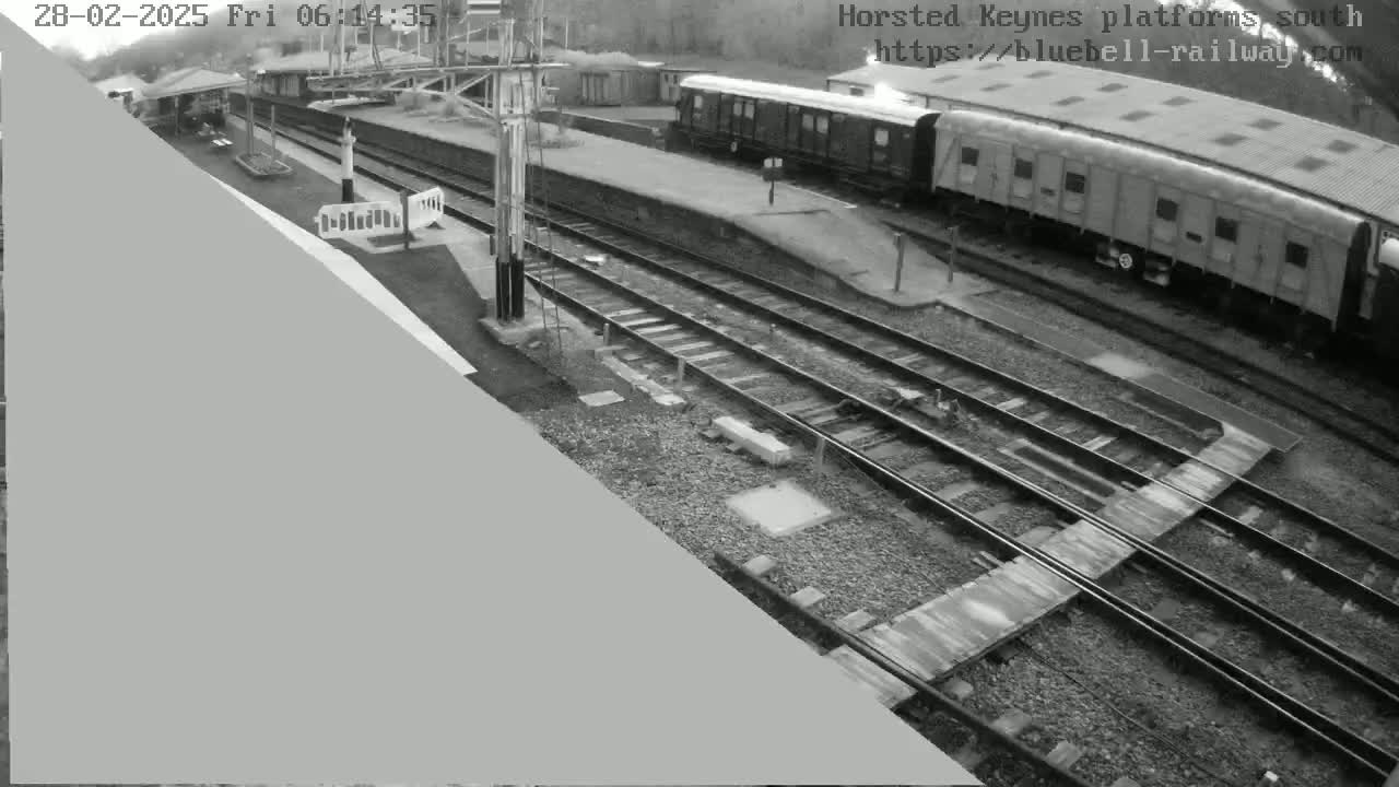 A high-angle grayscale view of a train station with railway tracks and a train parked at the platform, under overcast conditions.