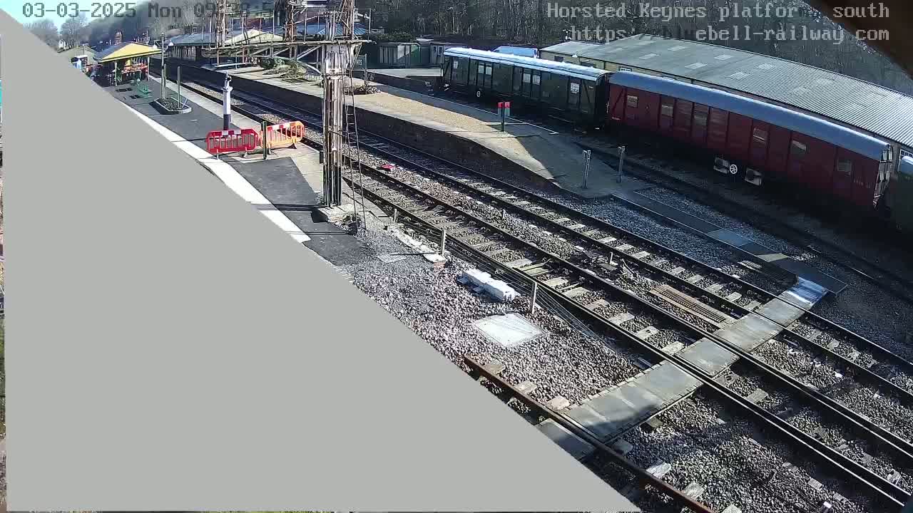 A sunny view of a railway station with train cars and multiple tracks, showing some construction or maintenance work in progress.