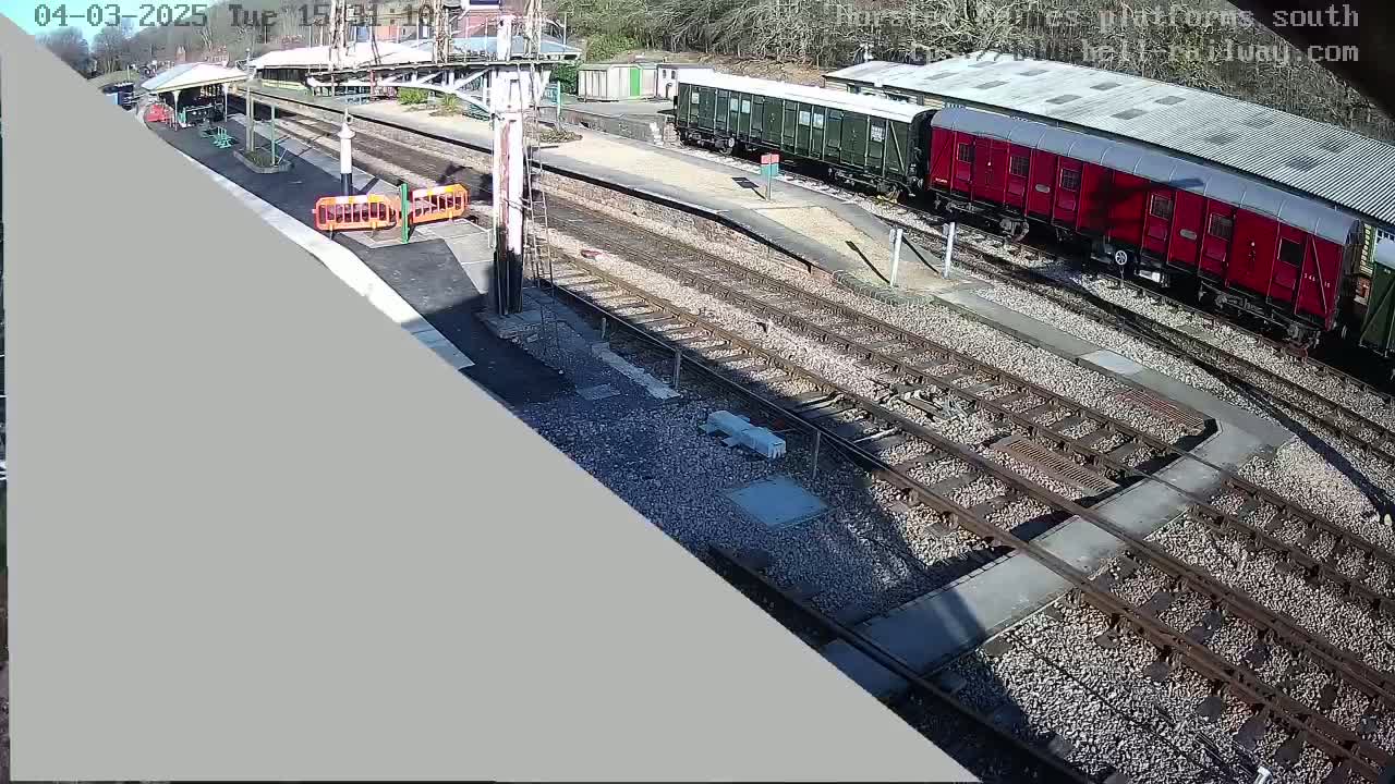 A high-angle view of a train station on a sunny day shows several train cars on the tracks, a platform, and a section of railway switching points.
