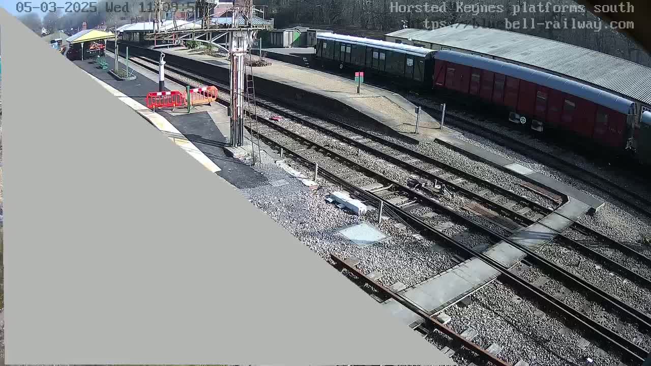 A sunny view of a train station with railway tracks, trains, and a partially visible platform.