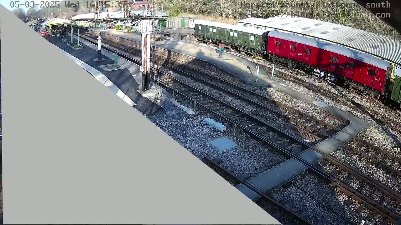 A sunny day at a train station shows several railway cars and tracks, a platform, and a station building.