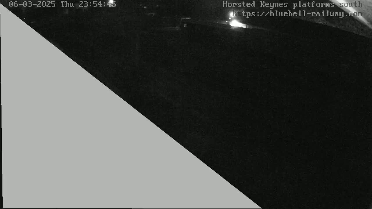 A nighttime, low-light image shows a dark area, possibly a train platform, with a gray triangle obscuring part of the view.