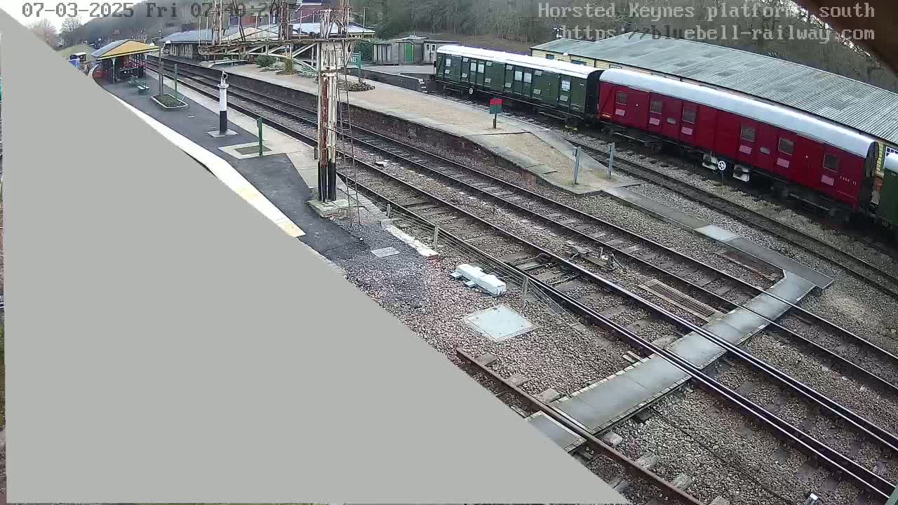A railway station on an overcast day with multiple train cars, tracks, and a platform visible.