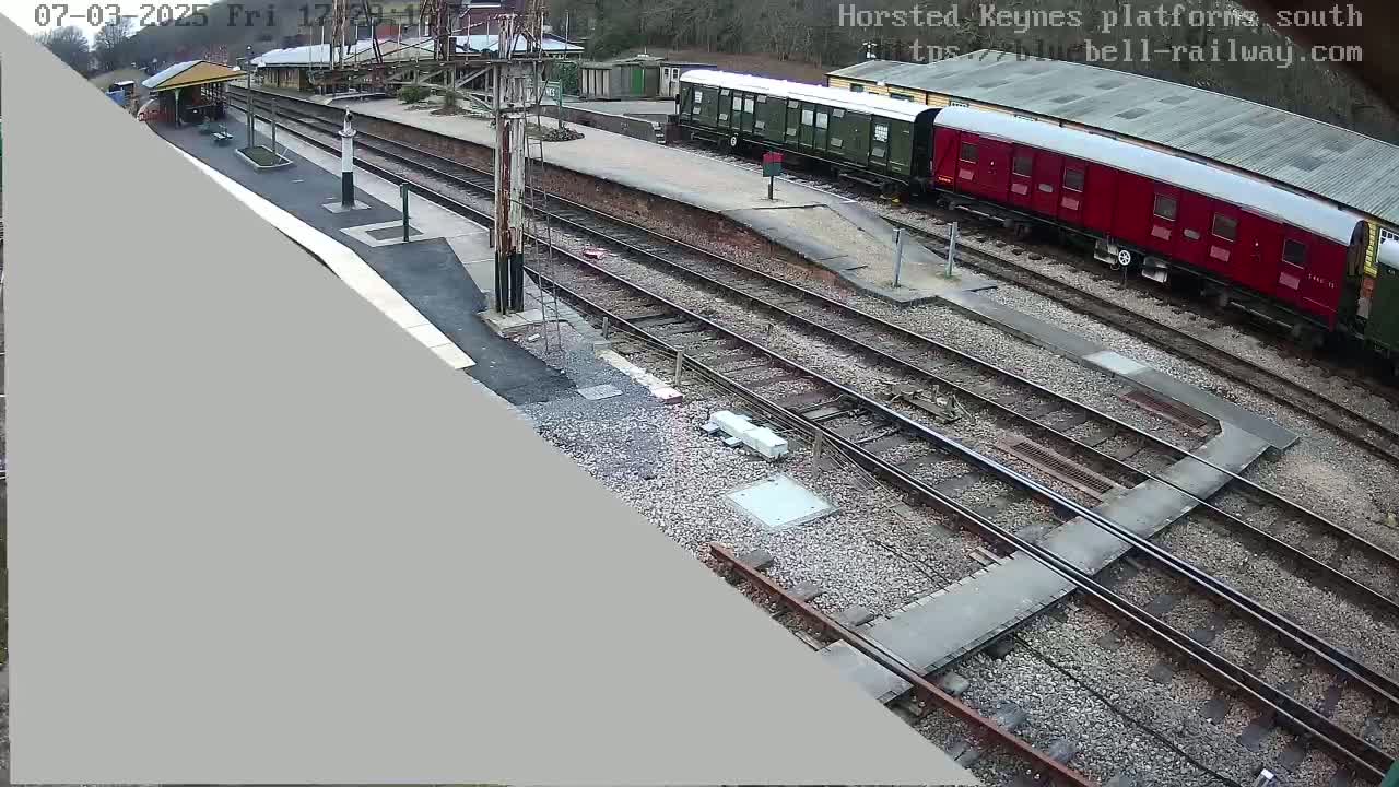 A high-angle view of a train station with several train cars, railway tracks, and a platform on an overcast day.