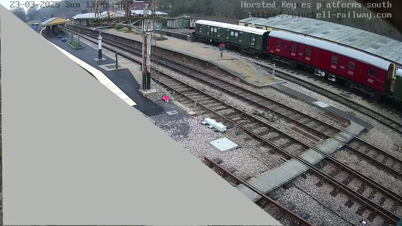 A high-angle view of a train station on an overcast day, showing multiple train cars and a network of train tracks.