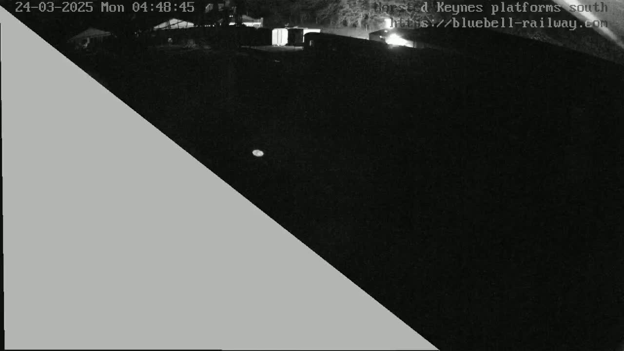 A nighttime, low-light view of a dark area with a few indistinct structures visible in the distance.