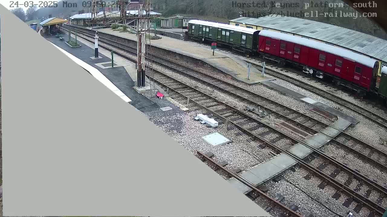A train station with several railway tracks, a partially visible green and a red train car, and a small covered waiting area.