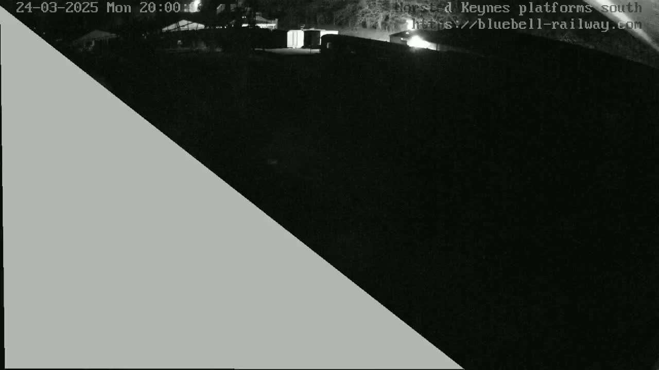 A nighttime, low-light view of a dark area with some structures visible in the distance.