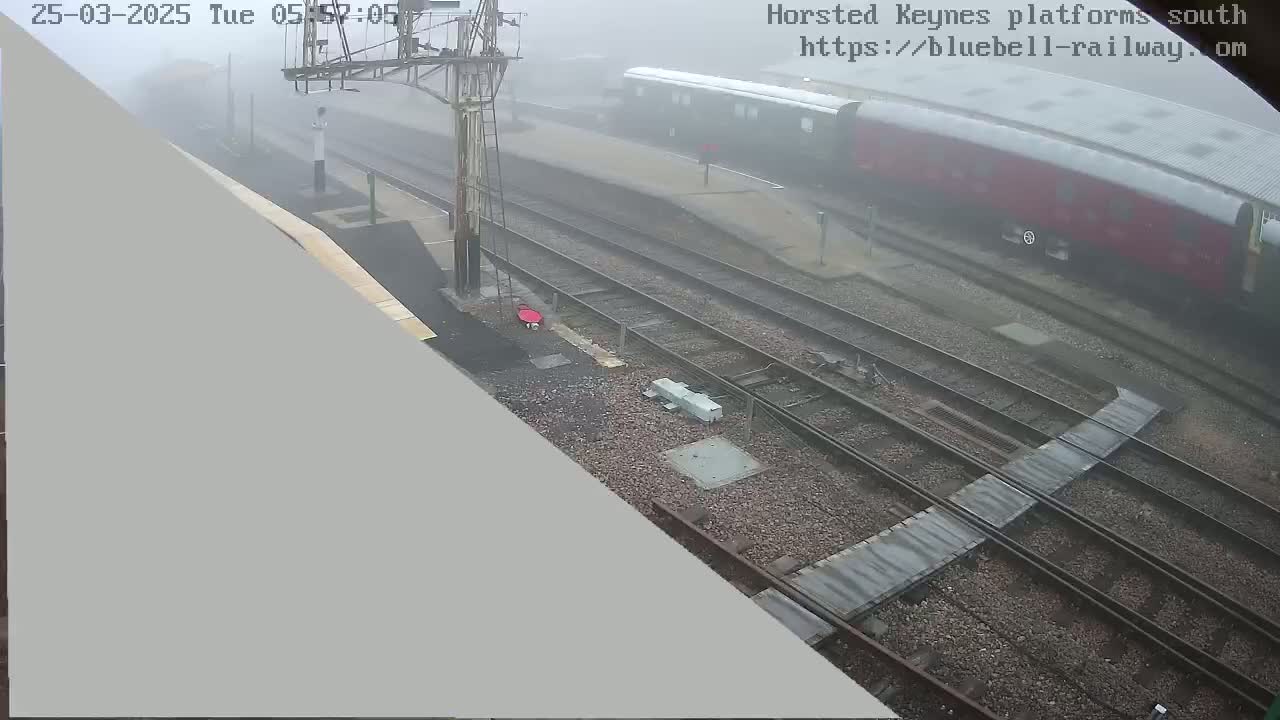 A foggy view of a train station with multiple train tracks and a partially visible red train.