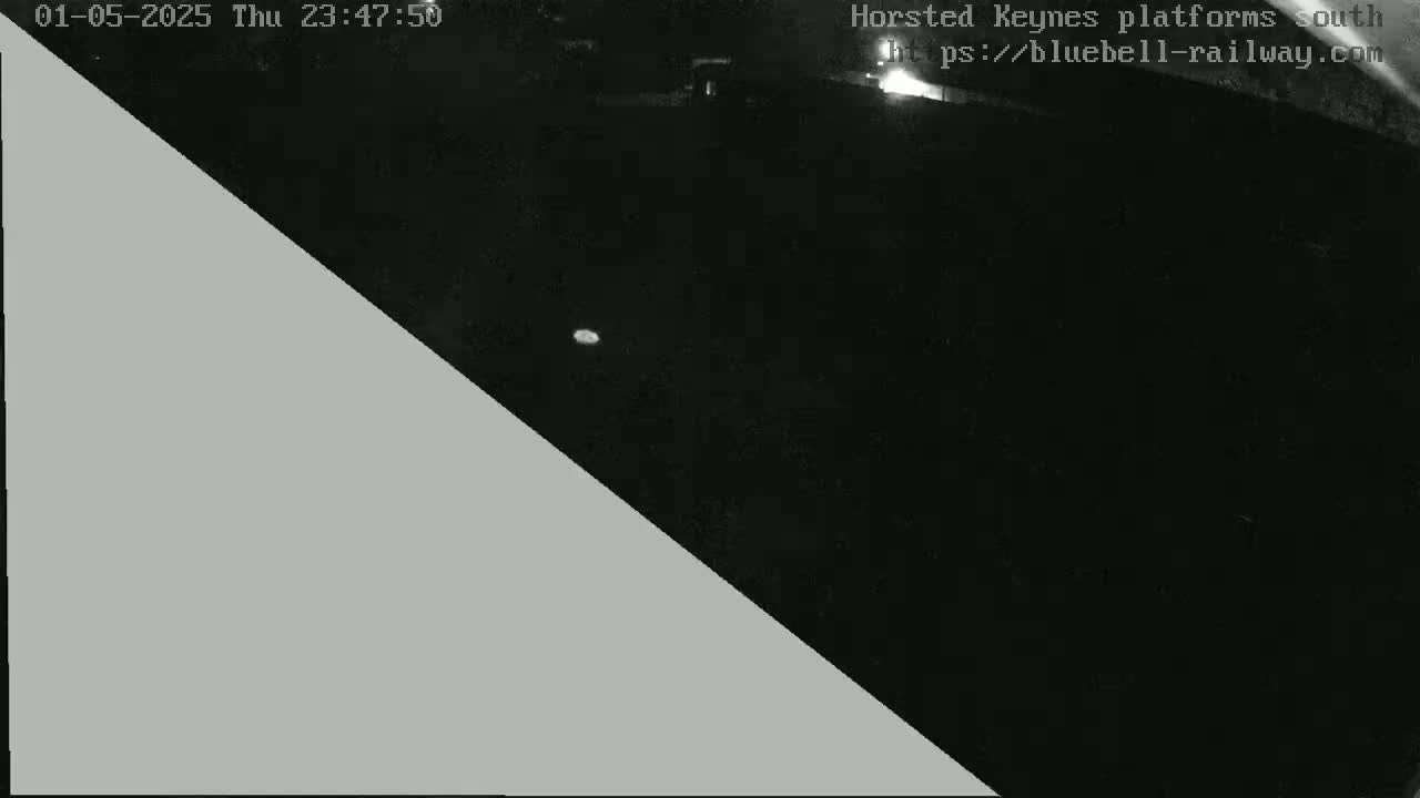 A nighttime, low-light image shows a dark area, possibly a train platform, partially obscured by a grey triangle.