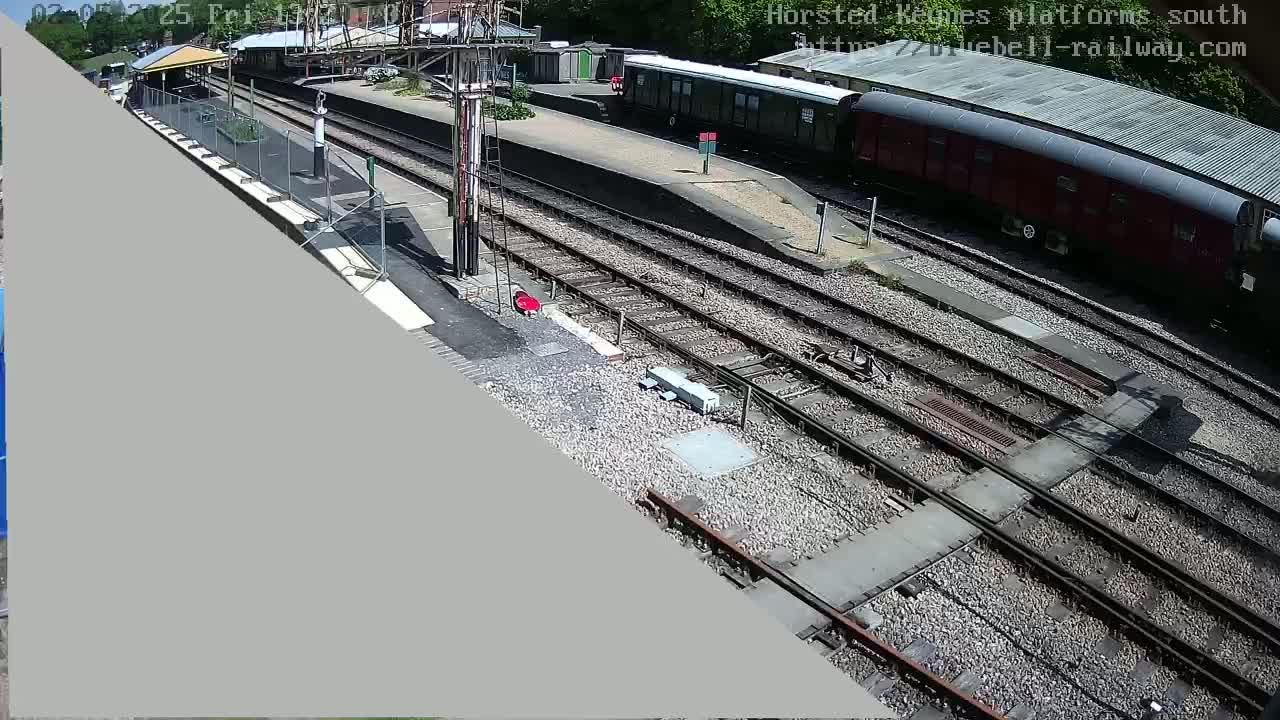 A high-angle view of a train station on a sunny day shows railway tracks, train cars, and a partially constructed platform.