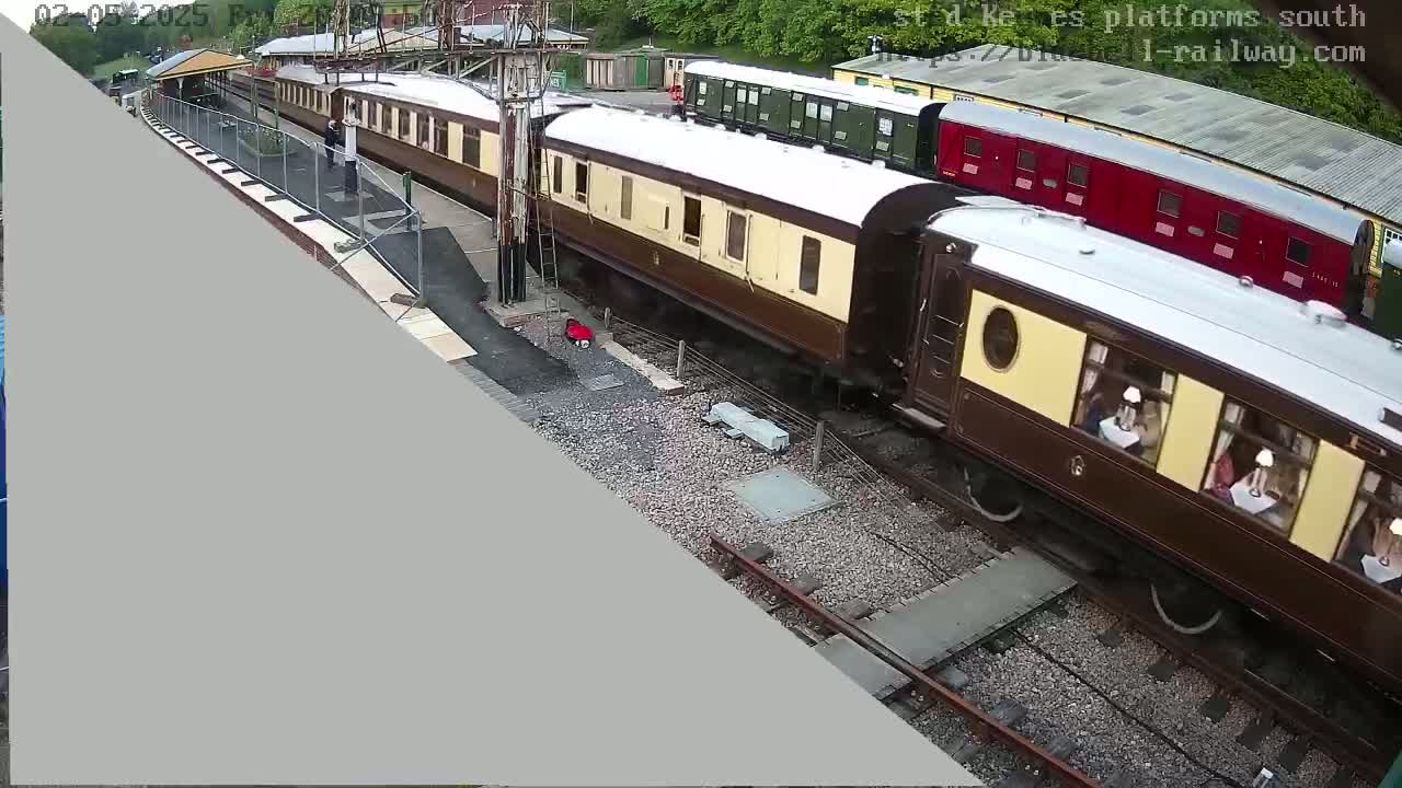 Several brown and cream passenger railway cars are parked on railway tracks in an outdoor setting under overcast skies.