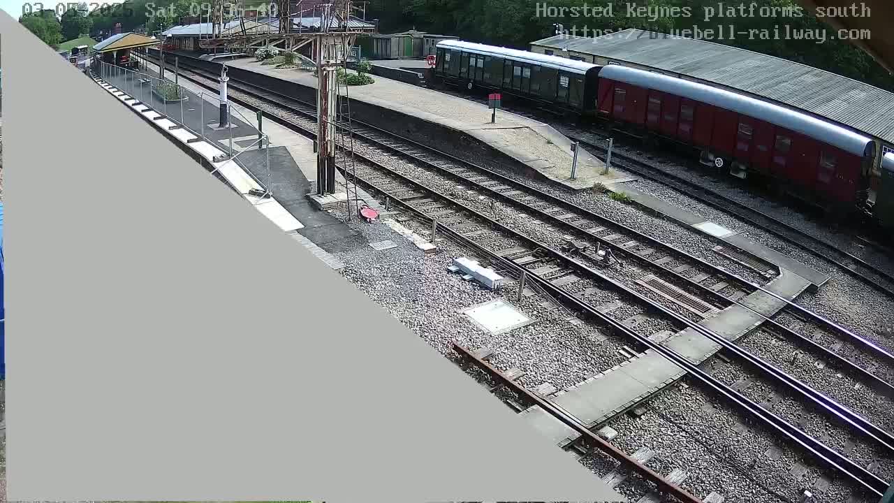 A railway station platform with multiple train cars and several sets of train tracks, on a sunny day.