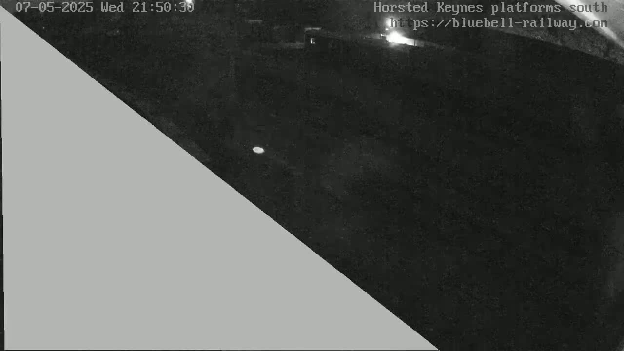 A nighttime, low-light image shows a dark, empty area, possibly a parking lot or field, with a gray triangle obscuring a portion of the left side of the frame.