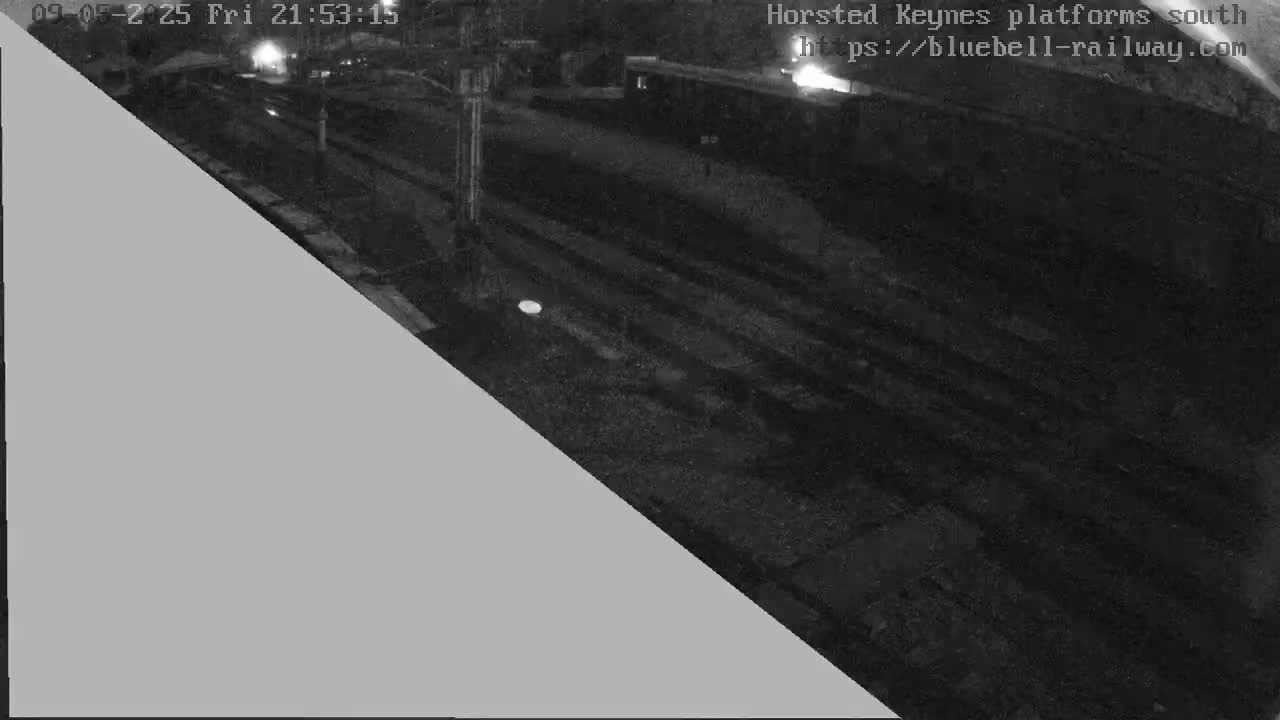 A nighttime, low-light view of a train platform with train tracks and a building visible in the background.