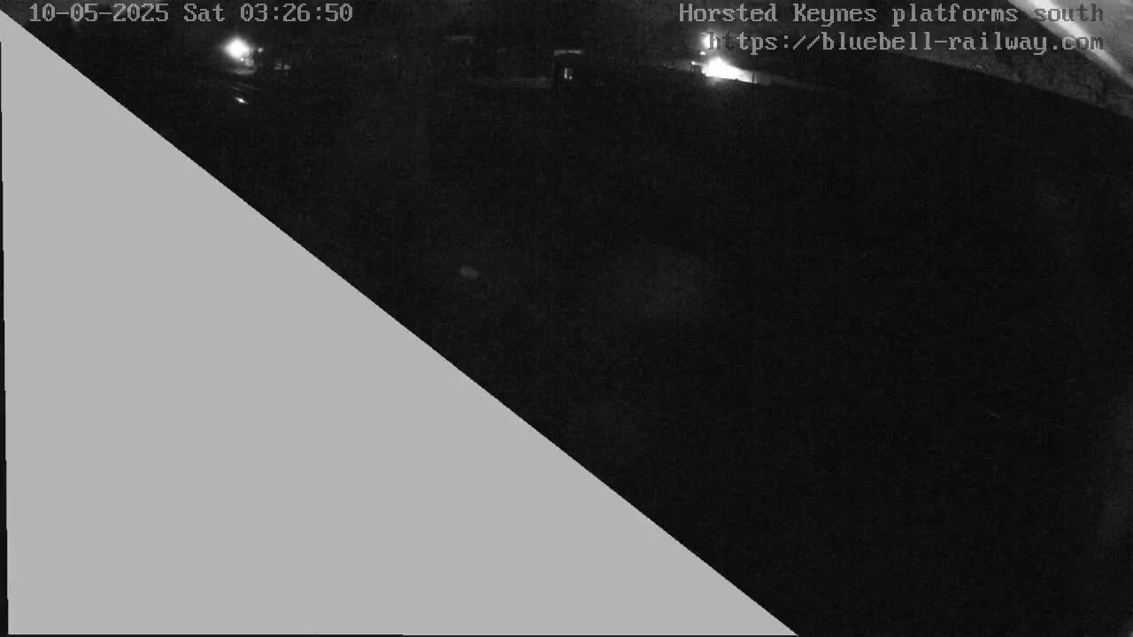 A nighttime, low-light view of a dark area, possibly a train platform, with a gray triangle obscuring part of the image.