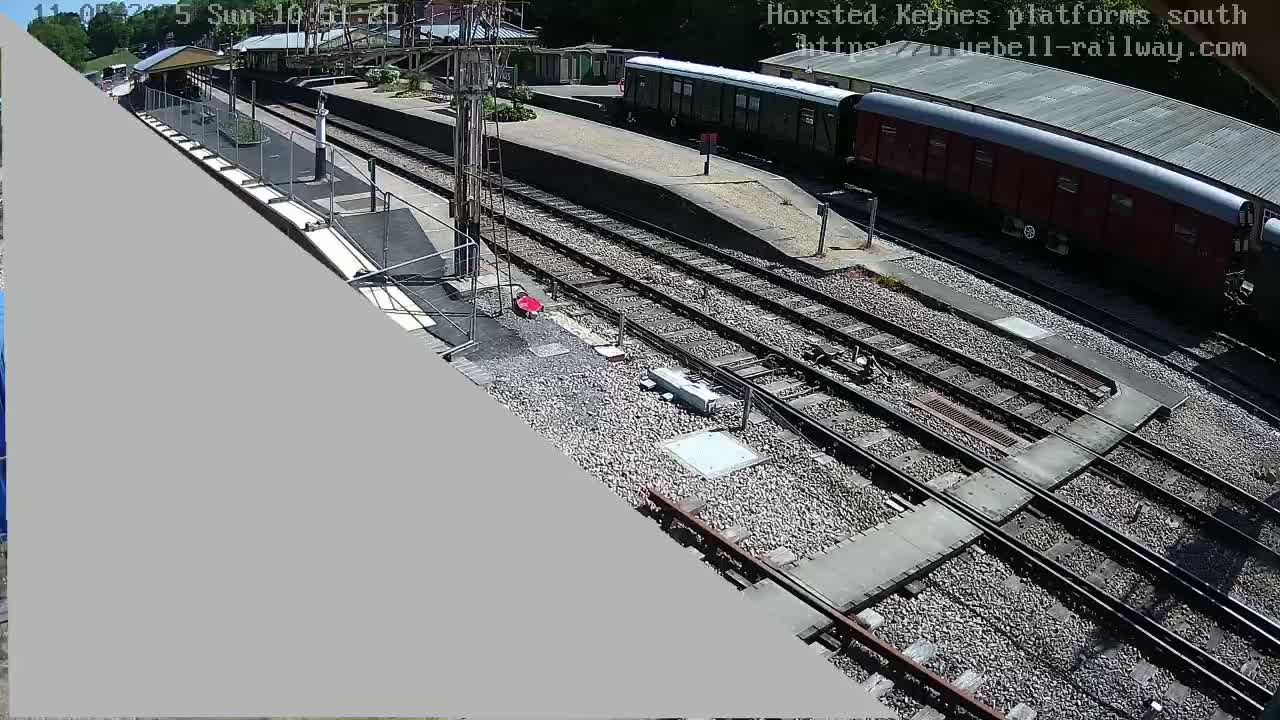 A sunny view of a train station platform with several railway tracks and two passenger cars parked on a siding.