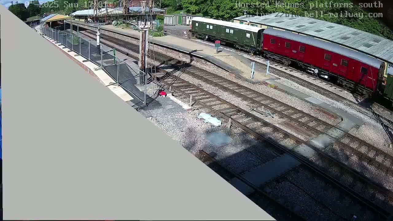 A high-angle view of a railway station on a sunny day shows a red and green train car parked on the tracks near a platform.