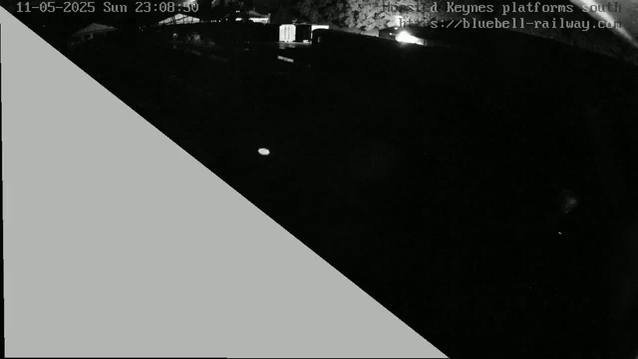 A nighttime, low-light image shows a dark area, possibly a train platform, with some indistinct structures visible in the distance.