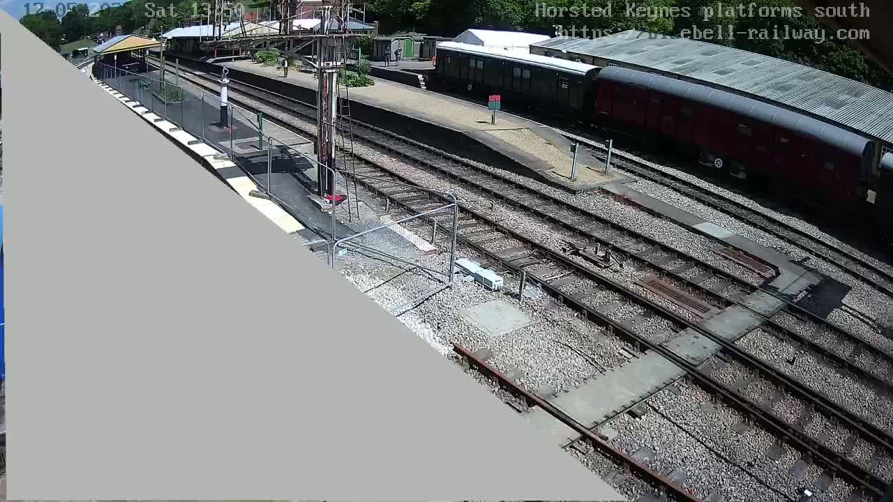 A high-angle view of a train station on a sunny day shows multiple train tracks and railway cars.