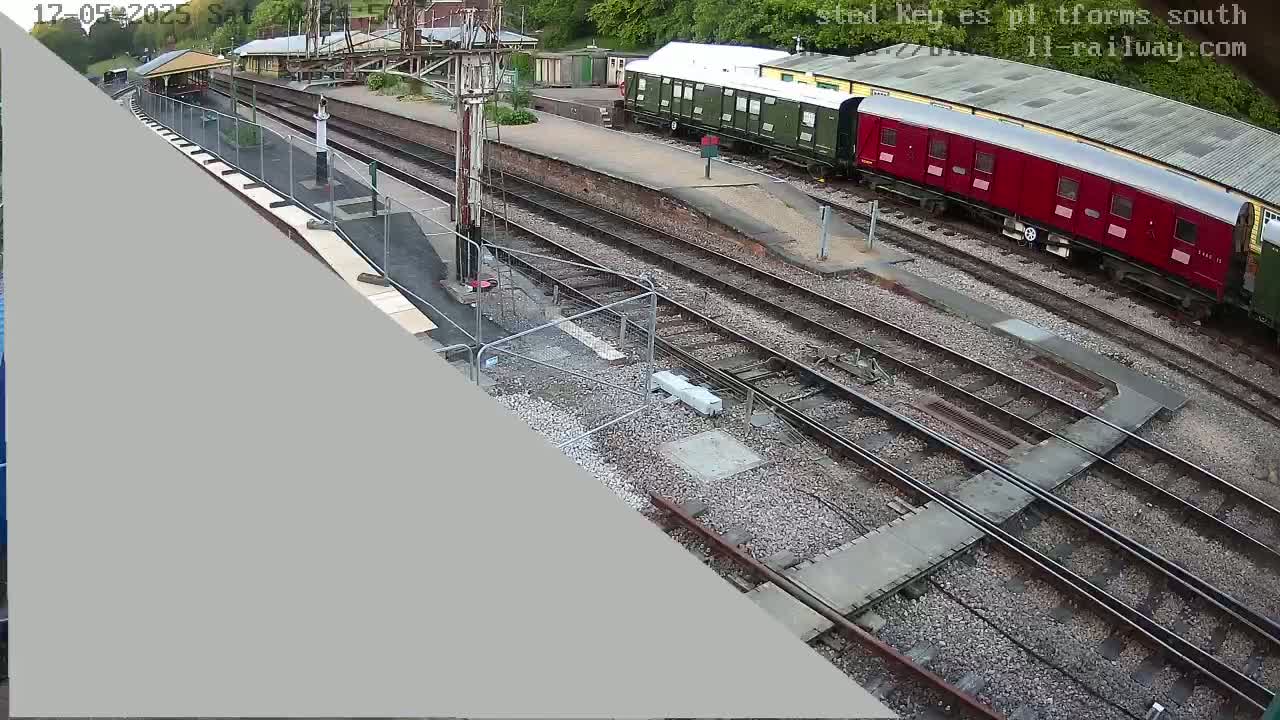 An overhead view of a railway station with multiple train tracks, a partially constructed platform, and several railway carriages, under an overcast sky.