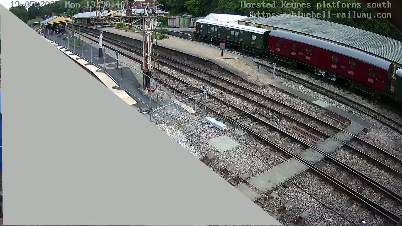 A high-angle view shows a railway station with multiple train tracks, a partially visible train, and a small building.