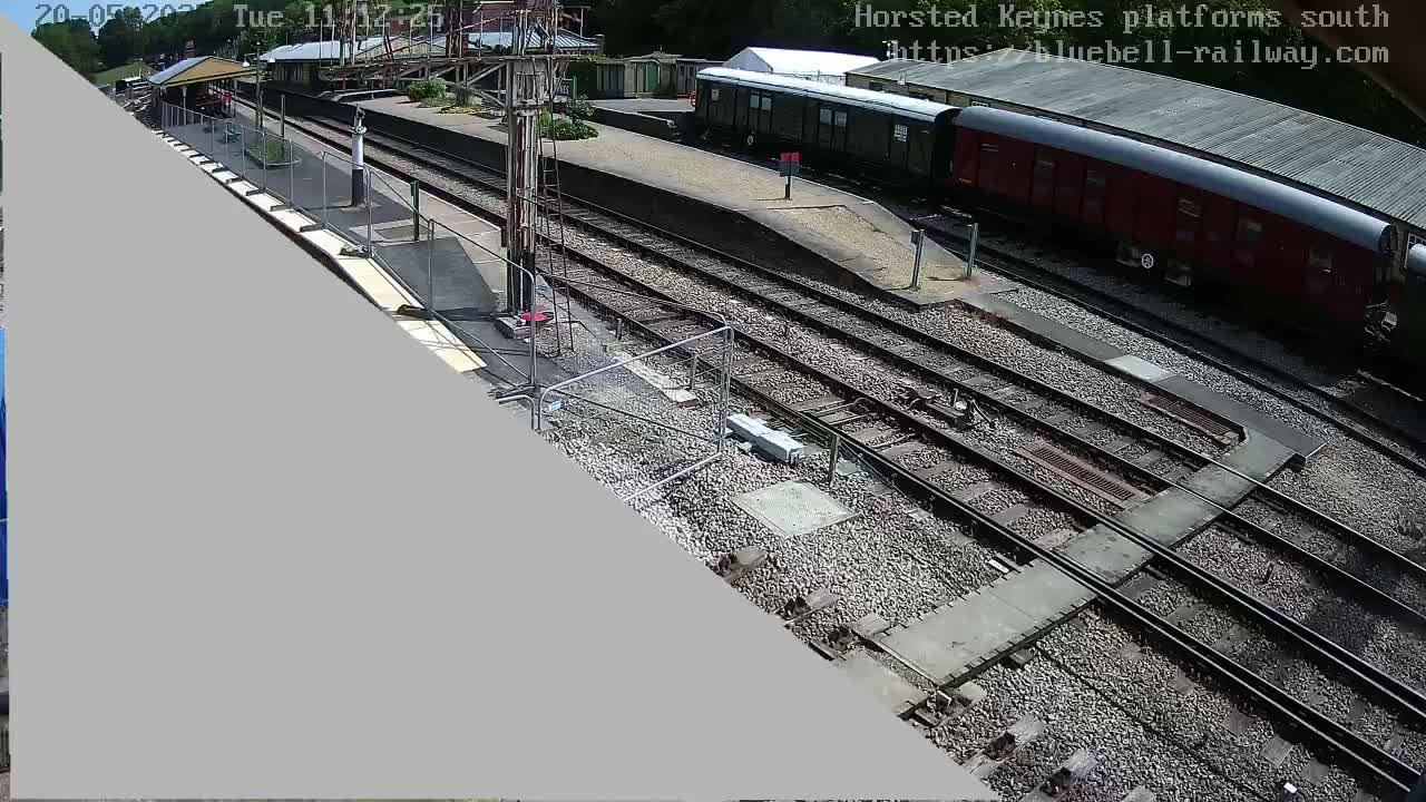 A high-angle view of a train station on a sunny day, showing railway tracks, a train, and a platform under construction.