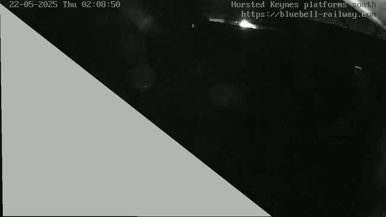 A nighttime, low-light image shows a dark scene, possibly a train platform, with a large gray triangle obscuring a portion of the view.
