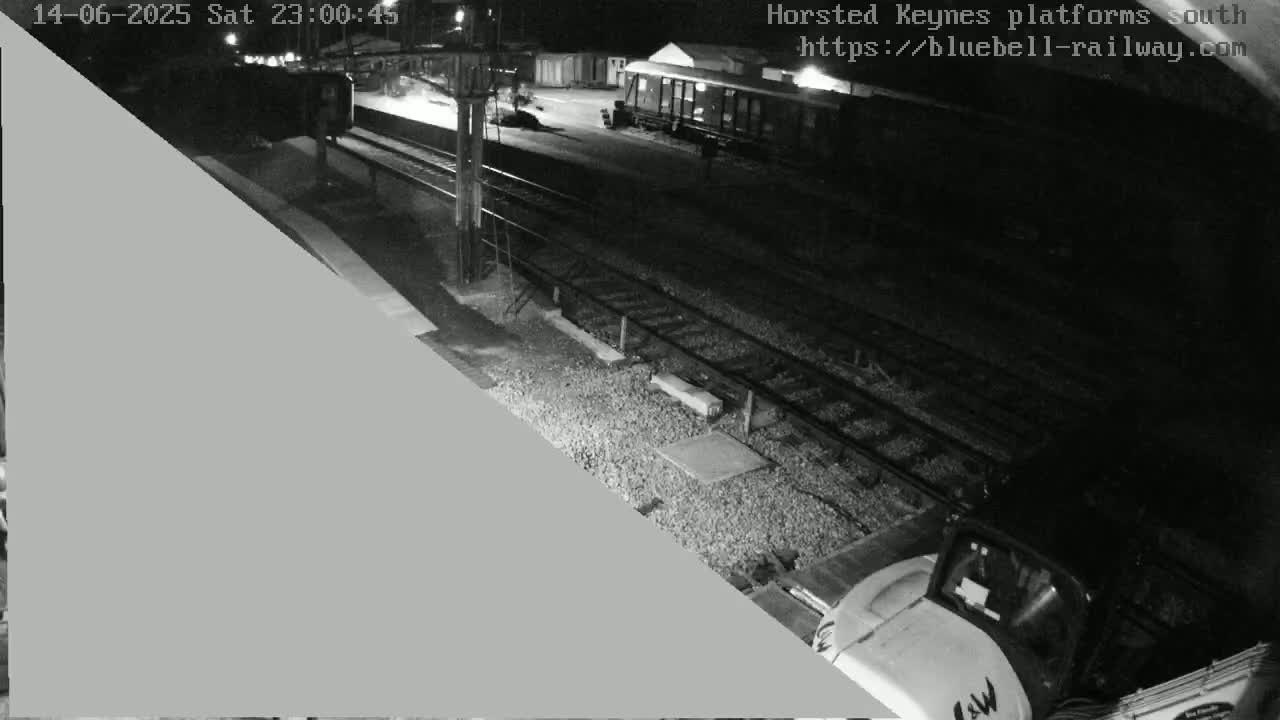 A nighttime, low-light image shows a dark scene, possibly a train platform, with a large gray triangle obscuring a portion of the view.