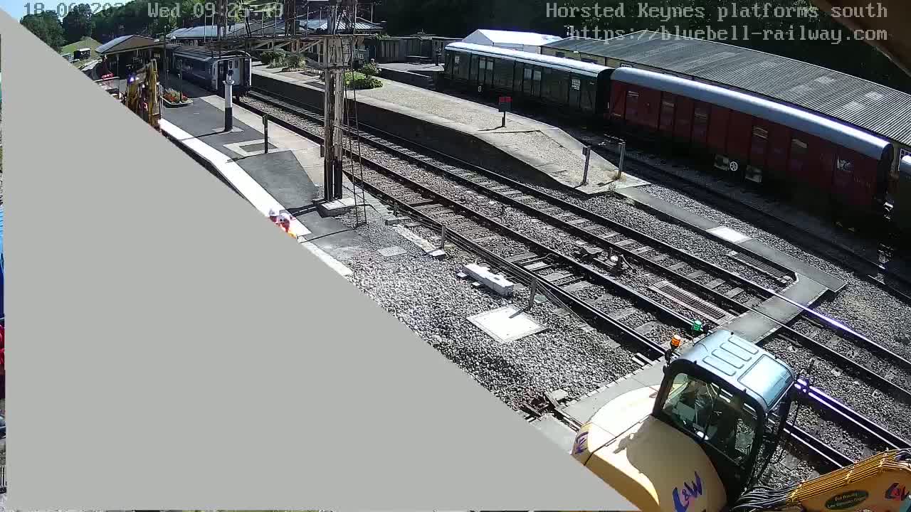 A sunny view of a railway station with train cars, railway tracks, and construction equipment.