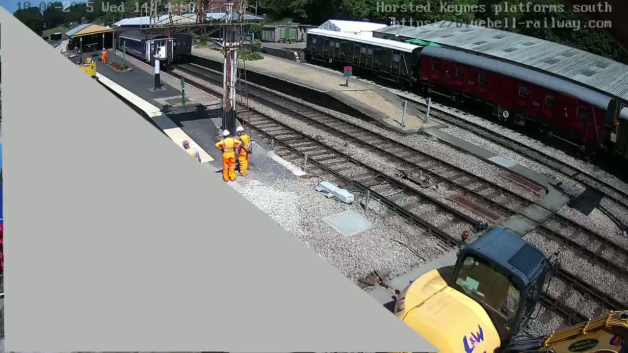 Construction workers are working on railway tracks near parked trains on a sunny day.