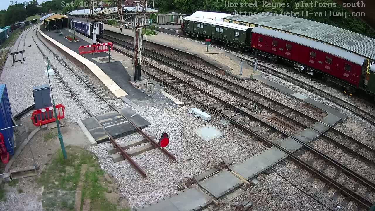 A high-angle view of a train station with several railway cars, tracks, and a platform under a partly sunny sky.