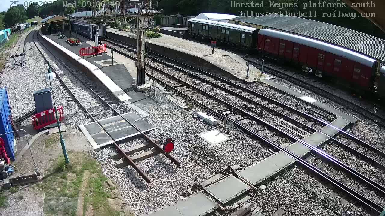 A railway station platform with several train cars and tracks, under sunny conditions.