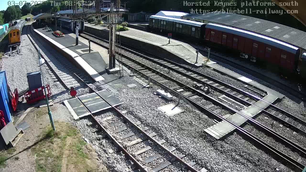 A sunny day at a train station with multiple train cars parked on various tracks, and a few train cars on the main line.