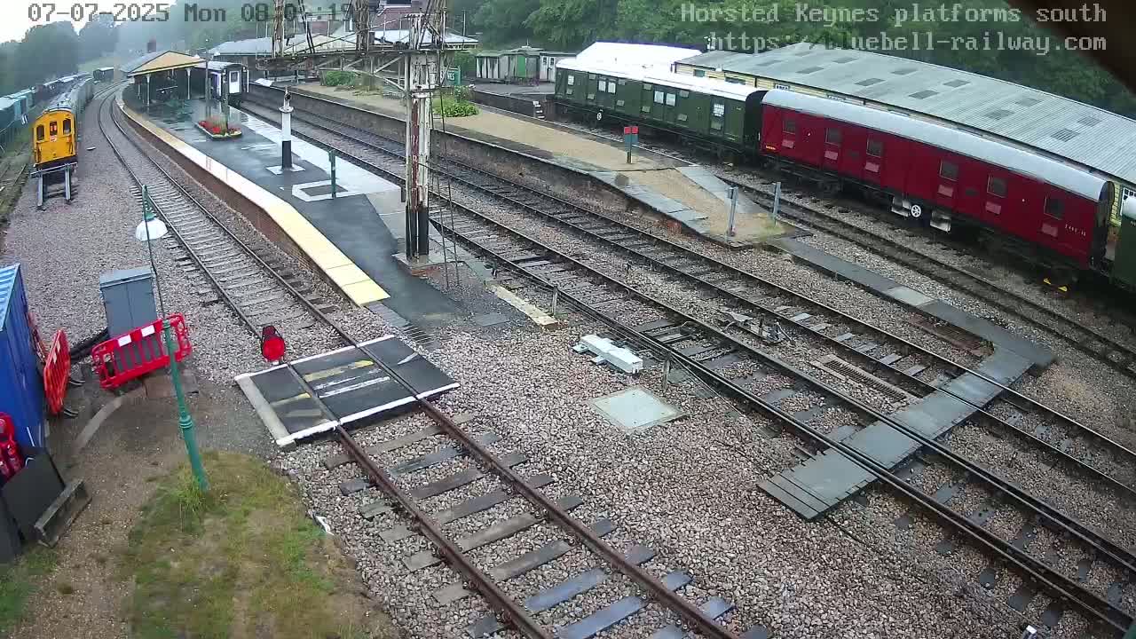A railway station with multiple train cars, tracks, and a platform under overcast skies.