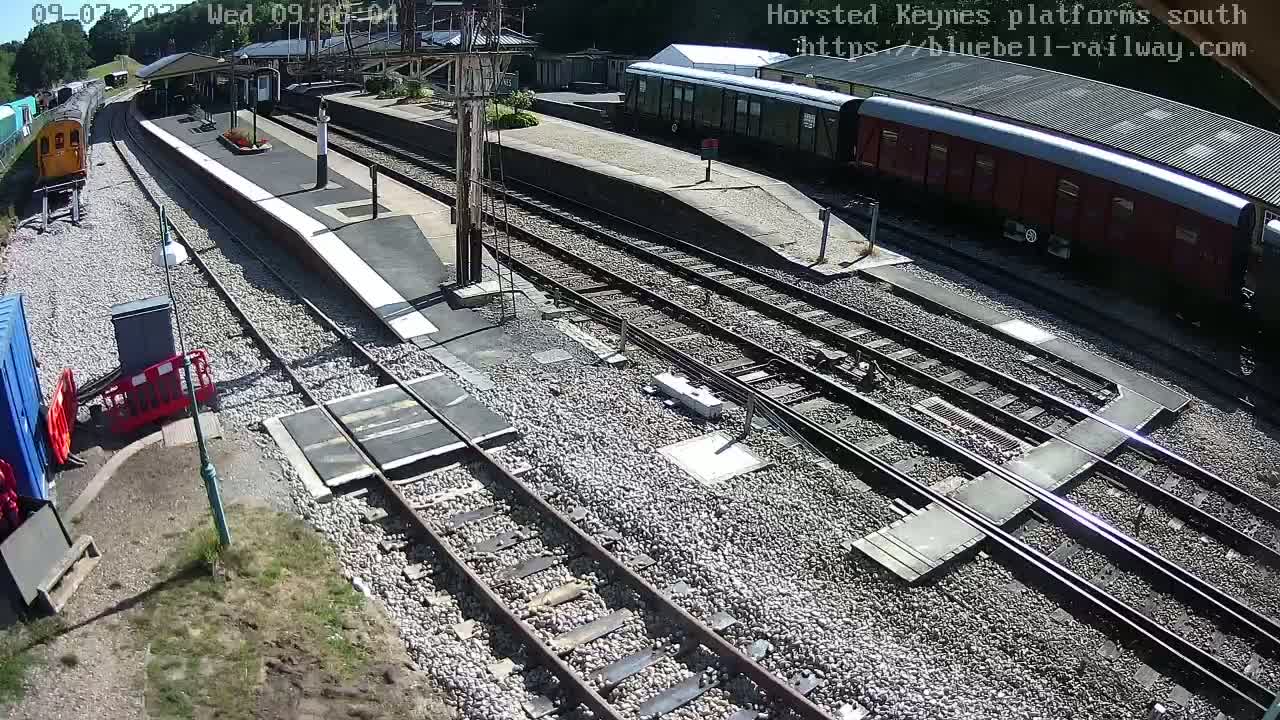 A sunny view of a train station with multiple train tracks, railway cars, and a platform.