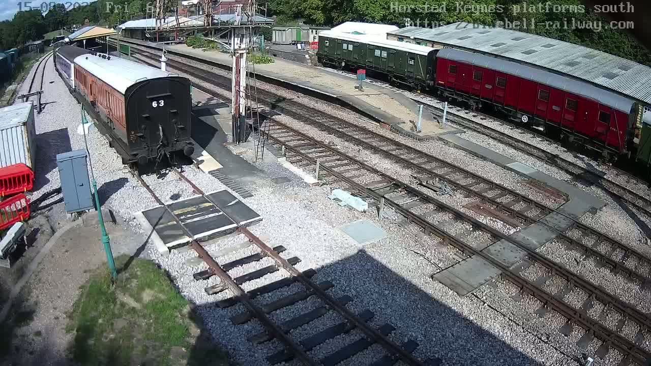A sunny view of a train station with multiple train tracks, railway cars, and a platform.