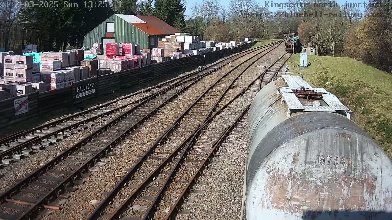 A sunny view of railway tracks branching out from a yard with stacks of building materials next to a green building.