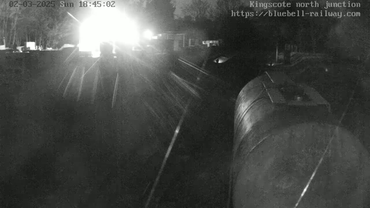 A nighttime, low-light view shows a large cylindrical object, possibly a tanker, with headlights in the background.