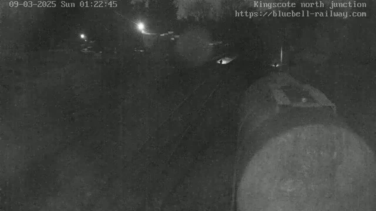 A dark, nighttime image shows a train partially visible in the lower right corner, with indistinct forms and faint lights in the background.