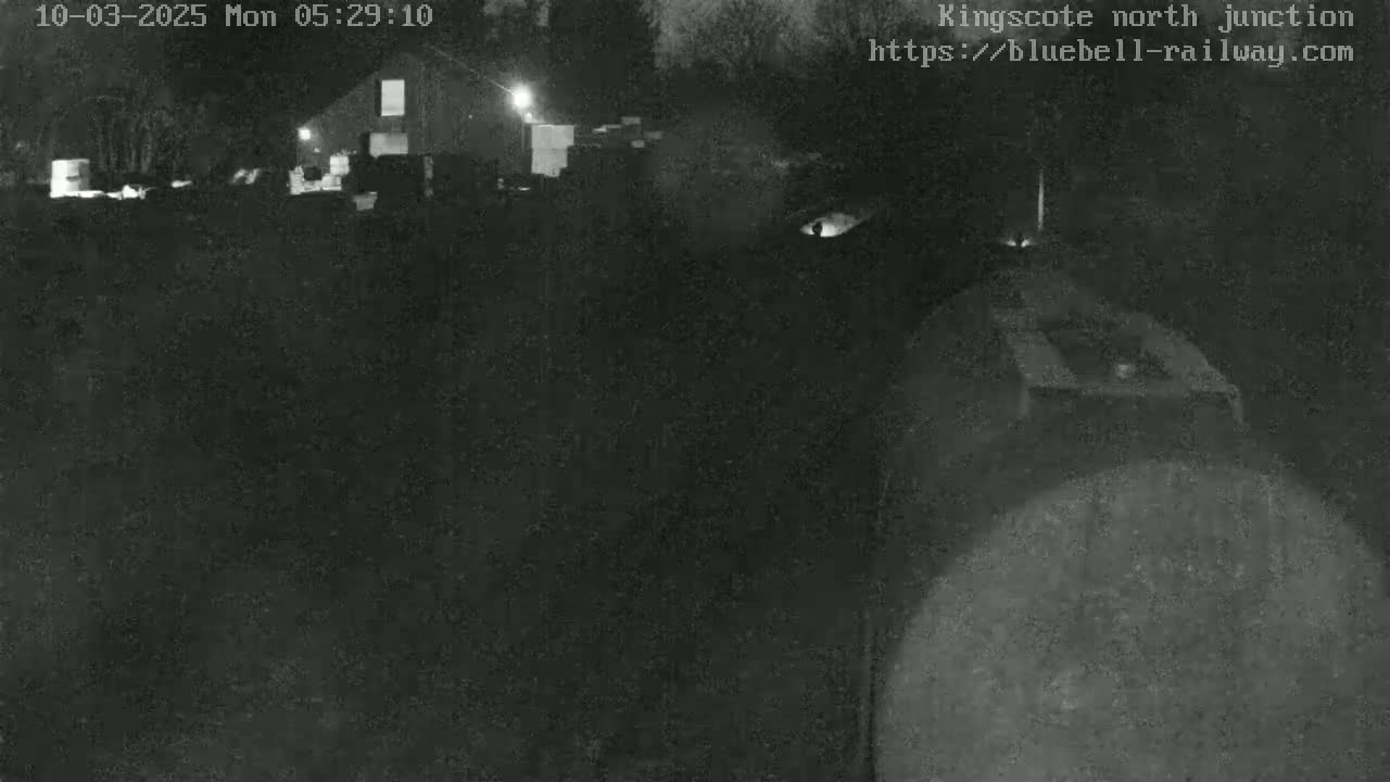 A nighttime, low-light image shows a dark, indistinct area with a building in the background.