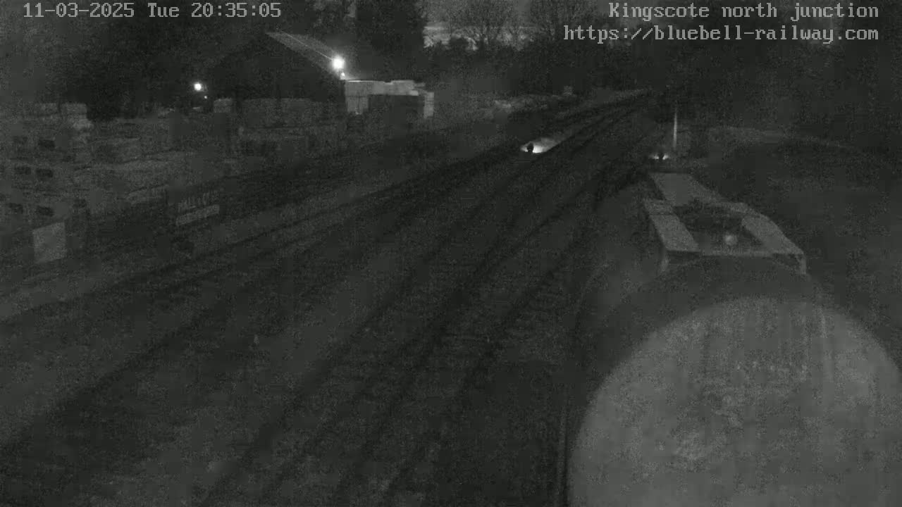 A nighttime view of a train on a track, with some structures and darkness surrounding it.