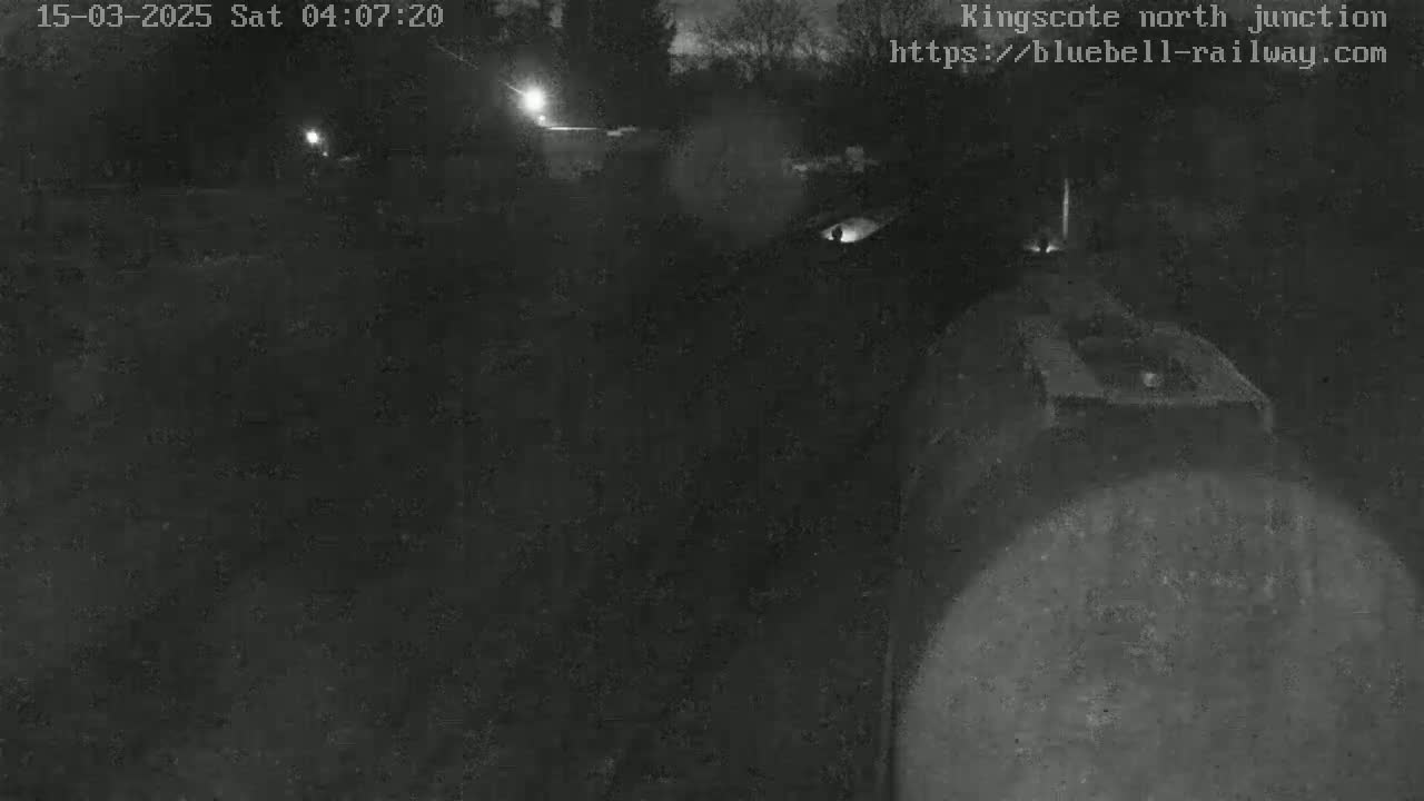 A nighttime, low-light view shows a dark, possibly railway, area with a large, dark object in the foreground.