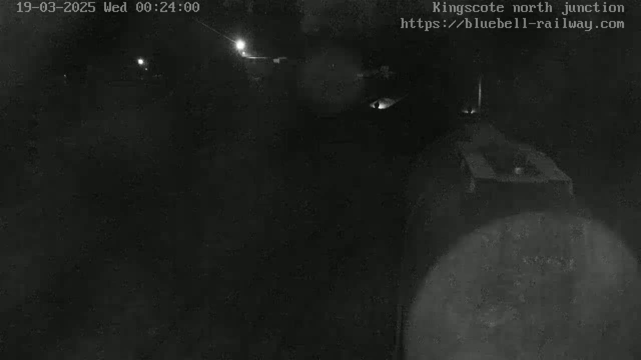 A nighttime, low-light view of a dark, possibly outdoor, area with indistinct shapes and faint light sources.