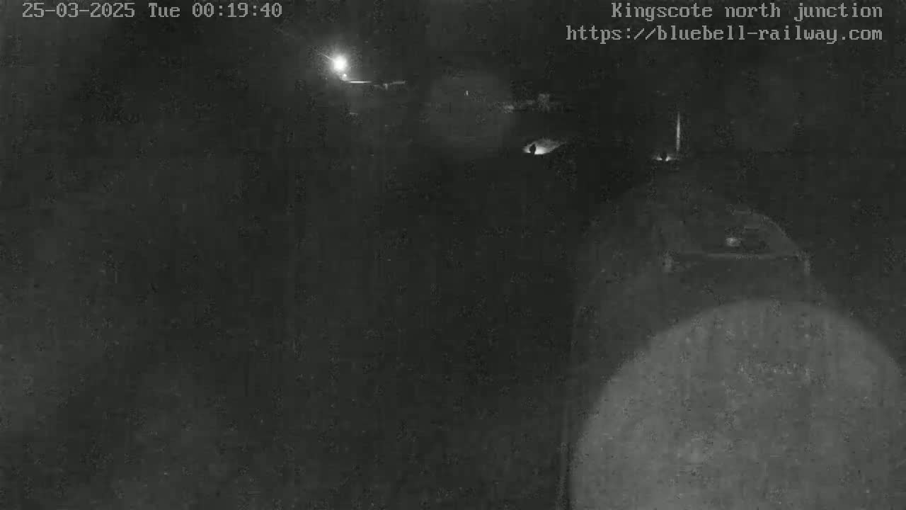 A low-light, nighttime image shows a dark area with a blurry object in the foreground, possibly a vehicle, under a dark sky.