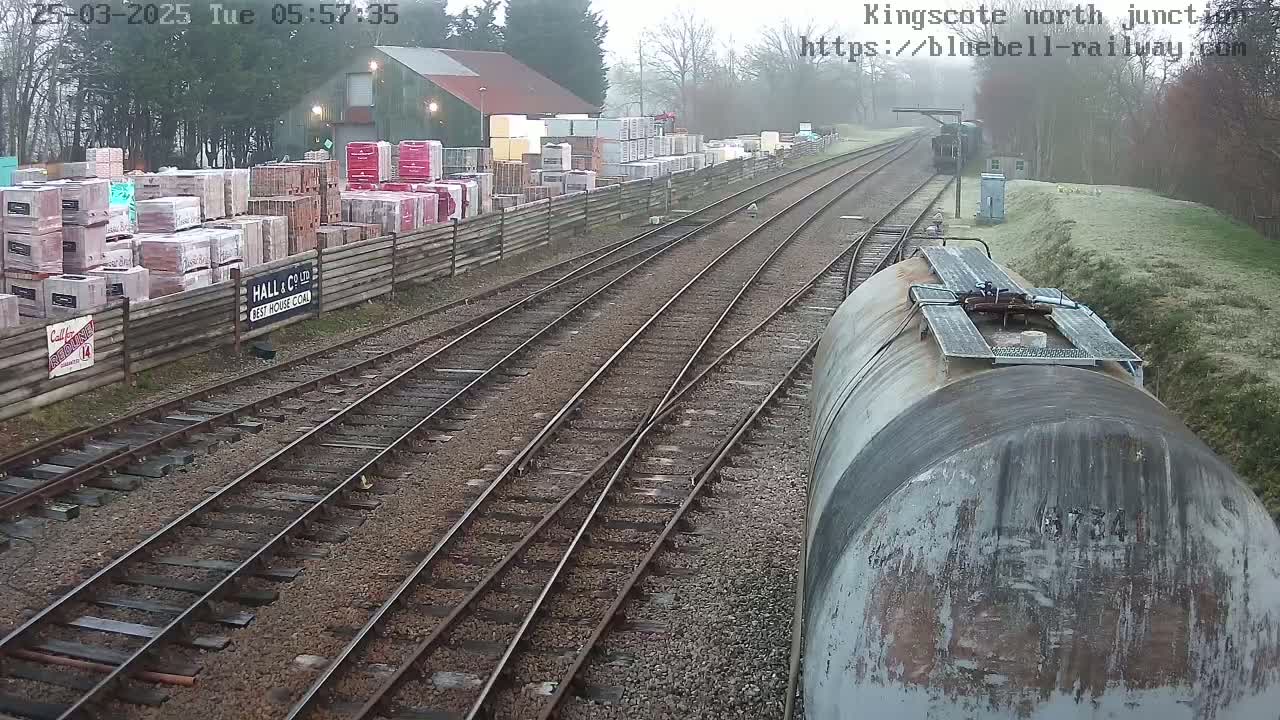 A view of a railway junction on an overcast day, with a train car in the foreground and stacks of building materials alongside the tracks.