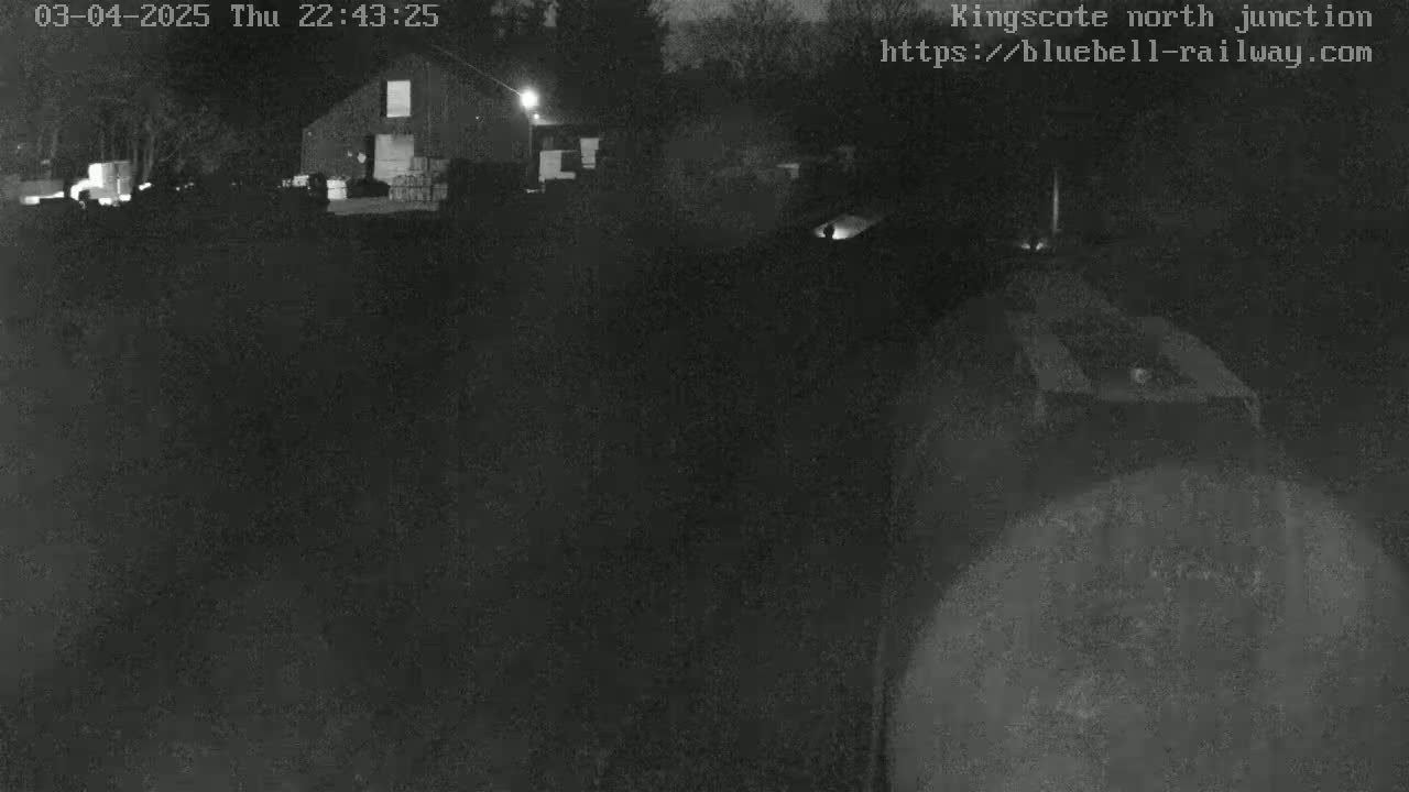 A dark, nighttime scene shows a building and surrounding grounds under low-light conditions.