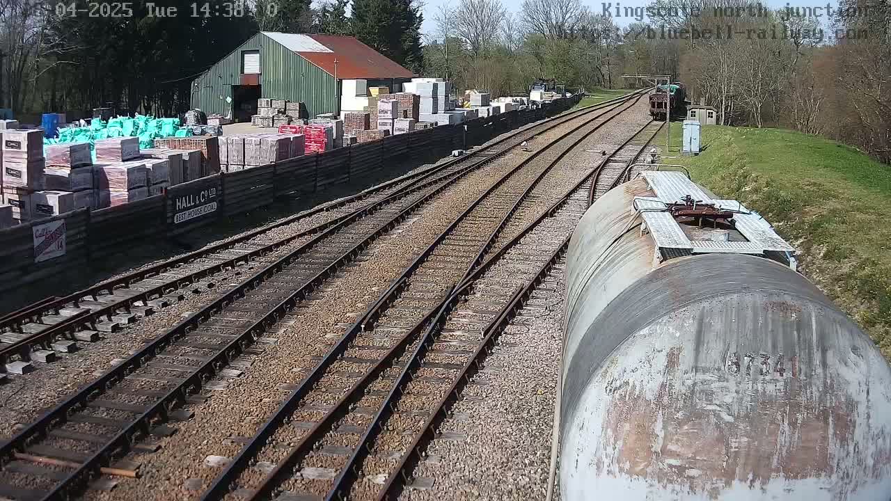 A train car views a sunny railway yard with multiple tracks, a building, and stacks of building materials.