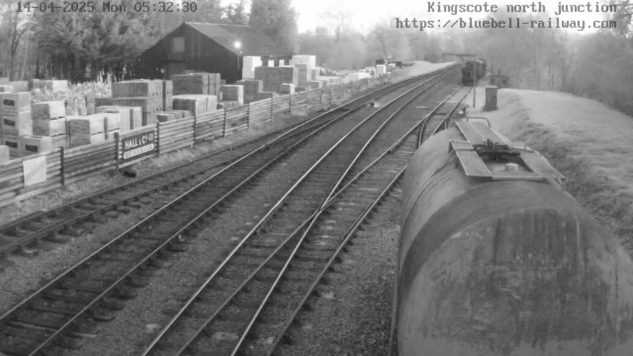 A railway junction on an overcast day, with a train and stacks of building materials visible alongside the tracks.